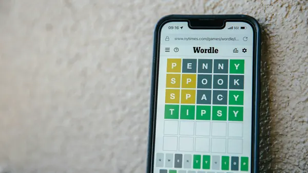 A phone against a stone wall showing a Wordle game, the fourth guess all green
