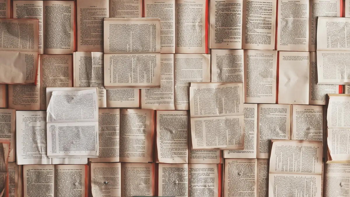 Dozens of open books laid flat side by side, filling the frame with printed pages