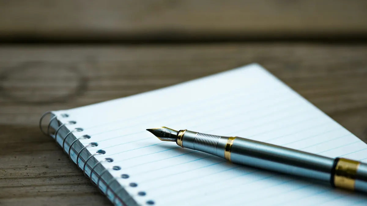 Fountain pen resting on a blank lined spiral notebook on a wooden table